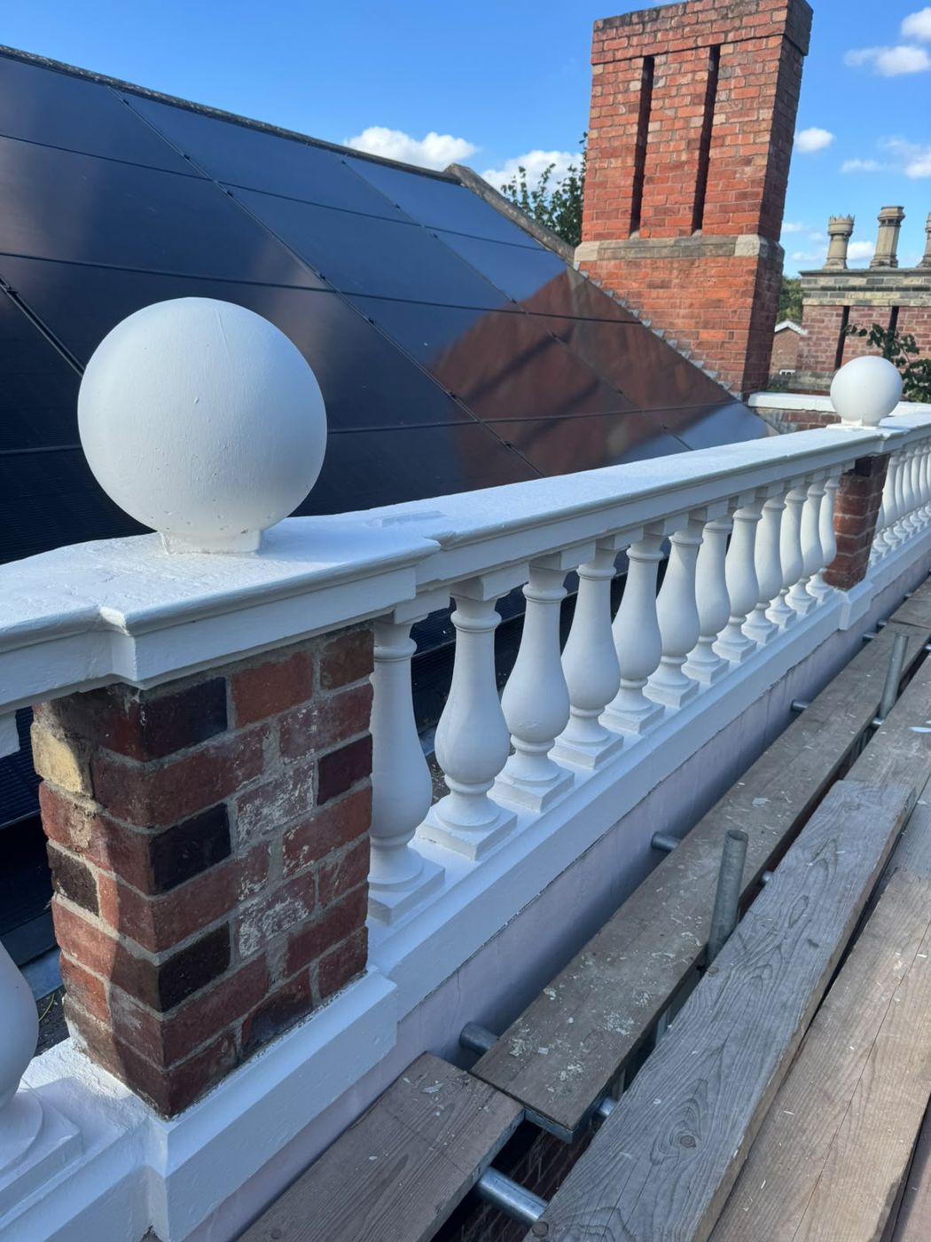 The same balustrade repainted white, with ball finials, beside new solar panels