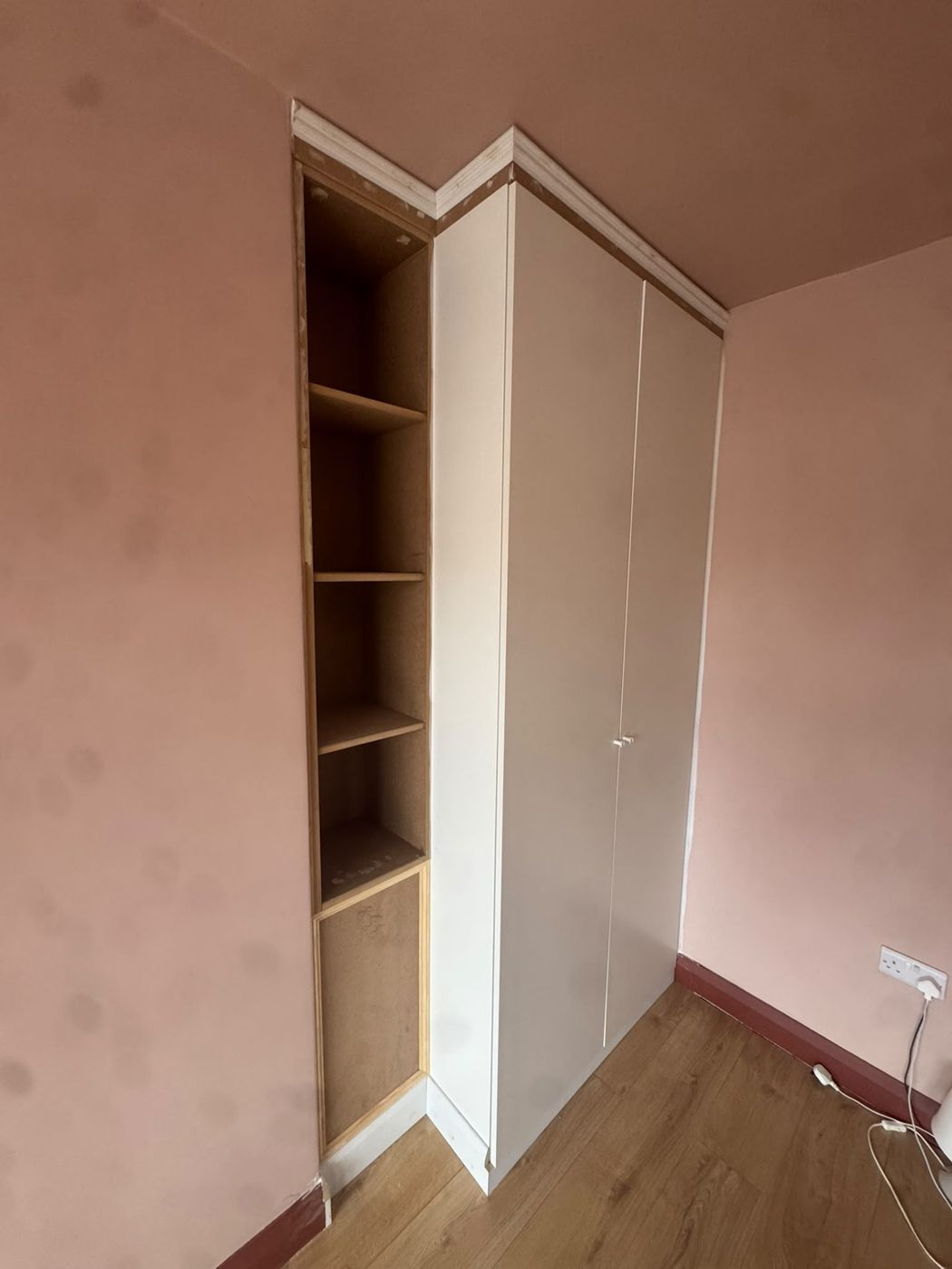 Shelving unit built beside a wardrobe, with trim fitted around the top before painting